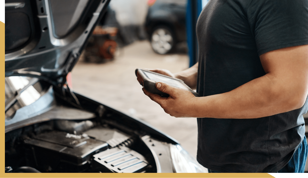 Factory Recommended Maintenance in Amarillo, TX at Panhandle Eurotech Automotive. Mechanic inspecting an engine with a diagnostic tablet.